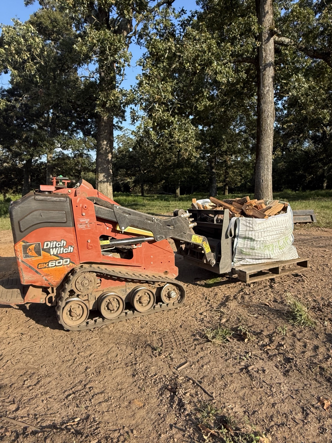 Oak Hill Firewood compact tracked loader carrying a large bag of firewood